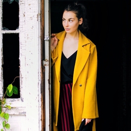 Jeune femme au manteau jaune mystérieusement tapie derrière une porte